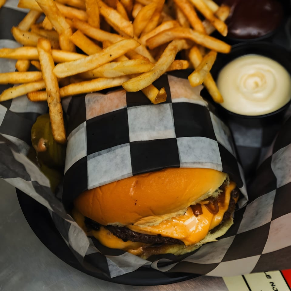 Cheeseburger with melted cheese, wrapped in checkered paper, served with golden fries and dipping sauces.
