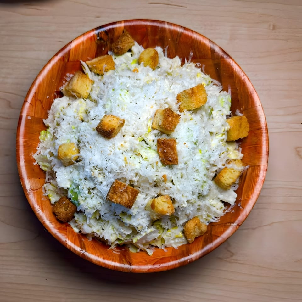 Caesar salad with shredded cheese and croutons in a wooden bowl on a light wood table.